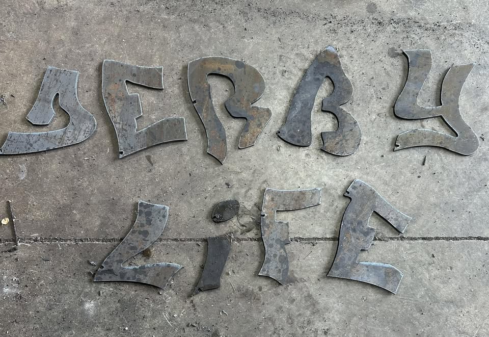 Plasma cut steel DERBY LIFE letters on the shop floor